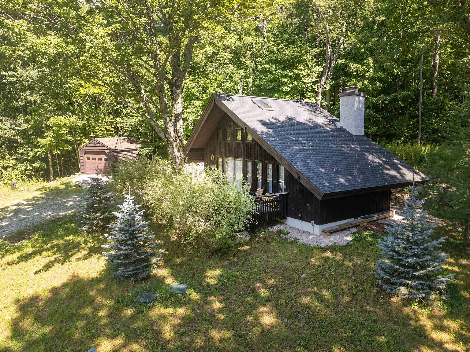 The chalet's steep roof and deck surrounded by green woodland in summer